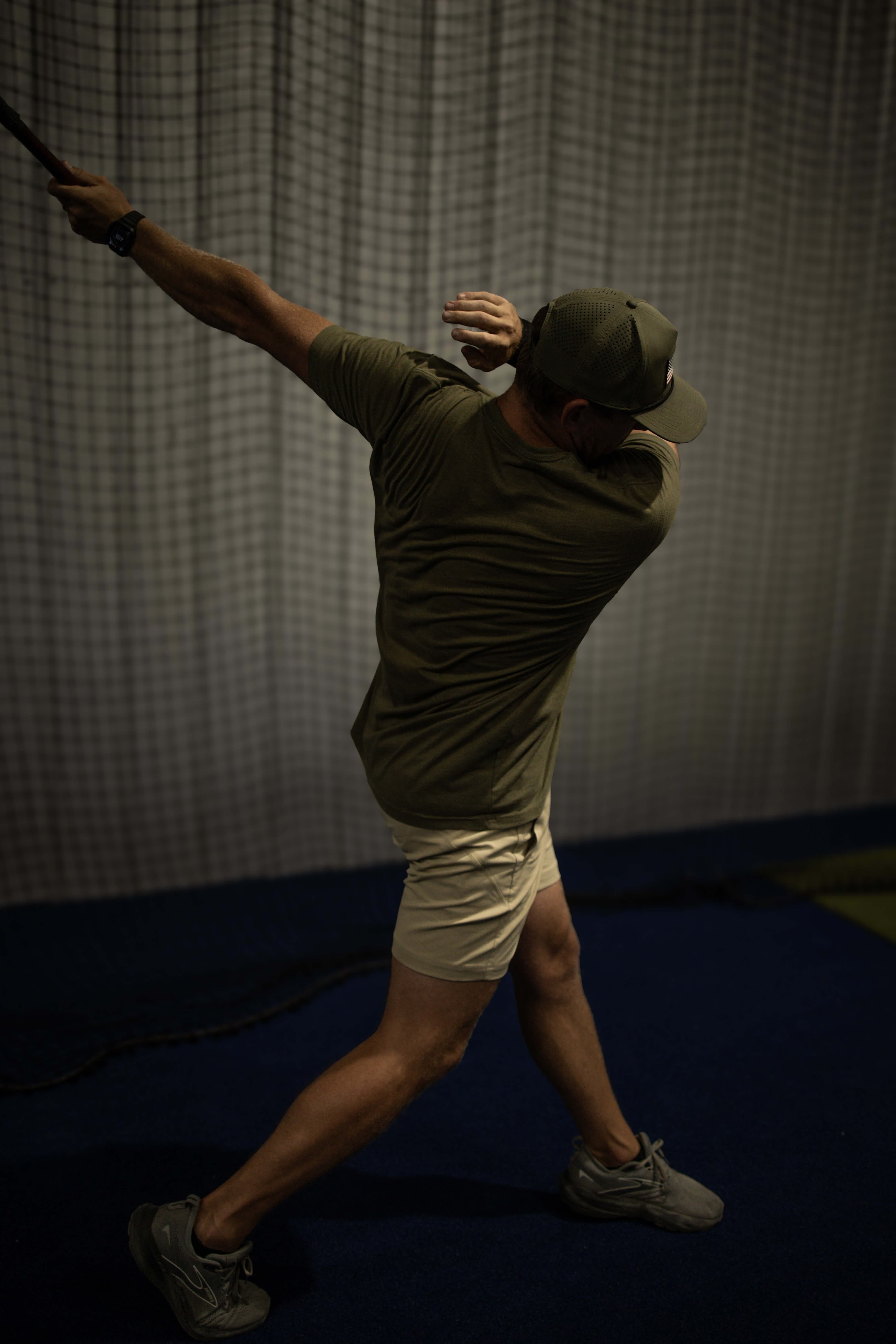 Hitter finishing a swing inside an indoor netted batting cage at Kingdom Built Performance